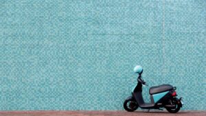 Blue scooter with a helmet on the handlebars against a blue background.