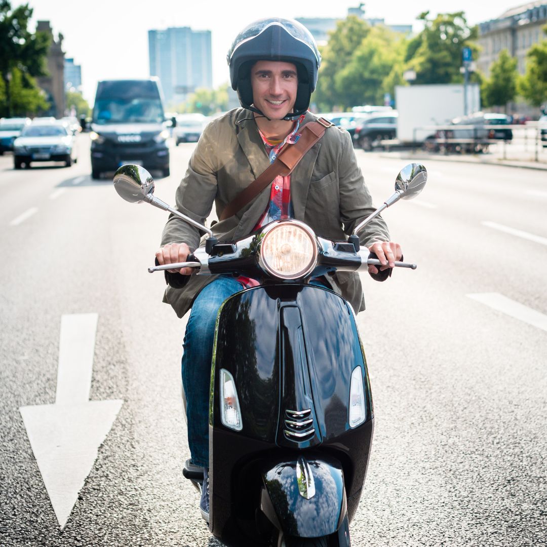 Man riding a scooter down the street, smiling.